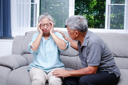 An elderly Asian couple sitting on the sofa at home A husband takes care of a wife who has a headache and is sick. Senior health conceptの写真素材