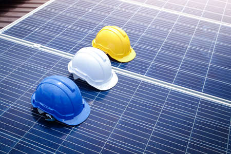 A safety helmet to prevent head bumps during work, a blue, white, yellow mechanic is placed on the solar panel. Concept of energy technology, work. copy spaceの写真素材