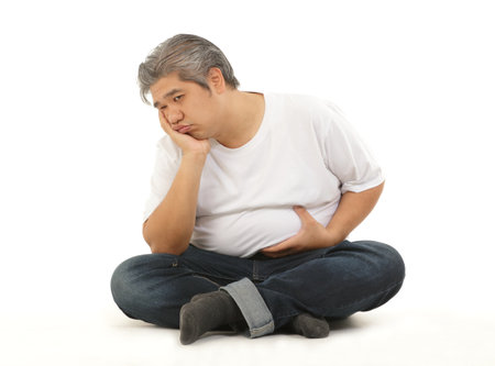 A fat Asian man wearing a white shirt sits stressed out due to hunger for food. Sitting on a white background. Concept of obesity problem, how to lose weightの写真素材