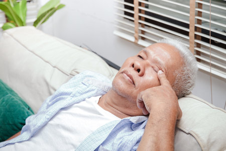 An elderly Asian man has eye pain. Sit on the sofa in the lounge. Senior health care conceptの写真素材