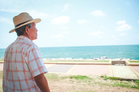 An elderly man wearing a hat looking at the beautiful seaの写真素材
