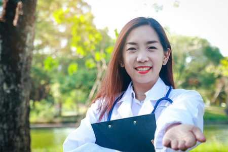 Beautiful young doctor standing in the garden Stretching his hand forward, smiling, happyの写真素材