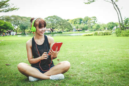 Beautiful Asian teenager likes to exercise Wear headphones, hold a tablet in the park.