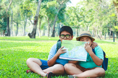An elementary Asian boy sitting on the lawn in the garden holding a map to study the information.の写真素材