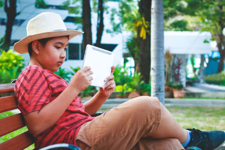 Asian boy Wearing a hat sitting on a chair playing a tabletの写真素材