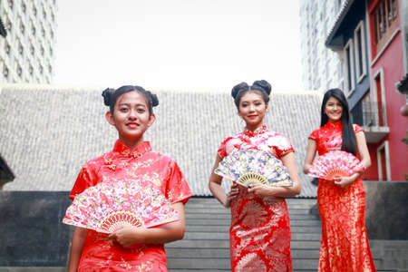 Beautiful Chinese female group in traditional red dress standing, sending a smile to welcome the Chinese New Year.の写真素材