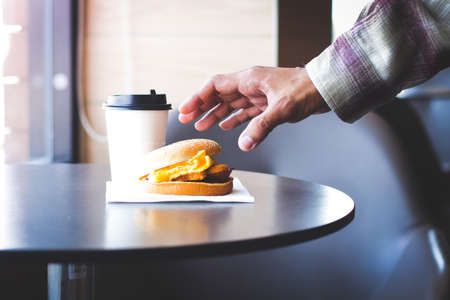 Asian male hands will pick up a hamburger placed on a wooden table with a cup of coffee. Is a food that is not good for healthの写真素材