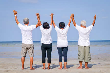 Happy group of elderly friends come to rest at the sea Standing, holding hands and facing the seaの写真素材