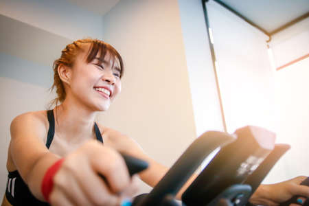 A beautiful girl who is exercising in the gym is riding a bike to control weight for good health.の写真素材
