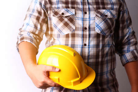 The young man works in construction, carrying a yellow safety hat. White backgroundの写真素材