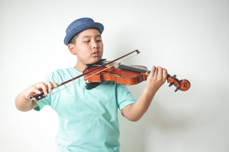 The little Asian boy wearing a hat is playing and practicing the violin in the white room.の写真素材