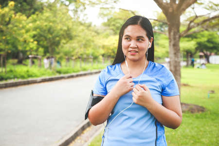 Fat woman, wearing headphones, music, walking, exercising in the parkの写真素材