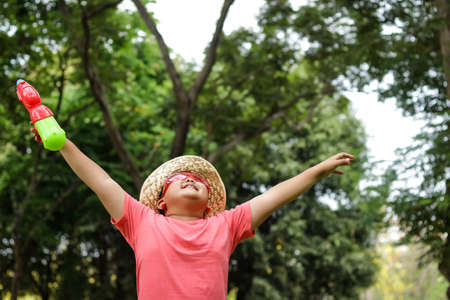 Asian boy wearing red glasses, wearing a hat, holding a gun, fresh water, standing, spread his hands in the garden. Songkran Festival in Thailandの写真素材