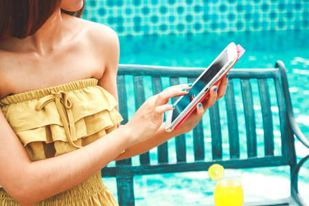 A beautiful woman sitting by the pool, she is playing the internet.