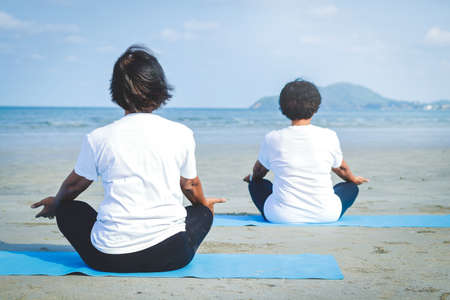 Two elderly women sitting on the sand, doing yoga by the seaの写真素材