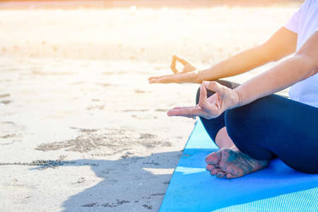 An elderly woman wearing a white shirt and doing yoga on the sand by the seaの写真素材