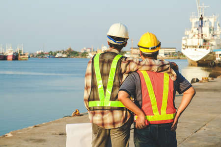 Engineers wearing white hats, carrying construction paper, hugging workers, wearing yellow hats Working at the portの写真素材
