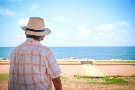 An elderly man wearing a hat looking at the beautiful seaの写真素材