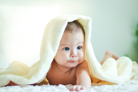 Baby boy lying in bed In which his head has a towel to cover the head to prevent coldの写真素材