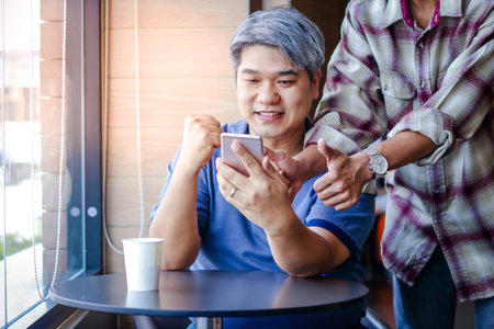 A young man sitting by the window in a restaurant Looked at the phone, lifted the arms, happyの写真素材