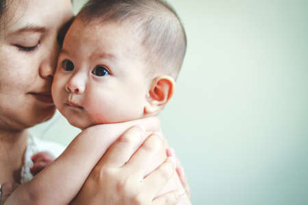 Asian girl mother hugging and kissing her baby sonの写真素材