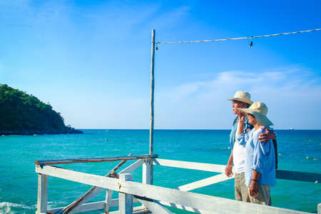 An elderly Asian couple standing hugging each other, happy at the sea.の写真素材