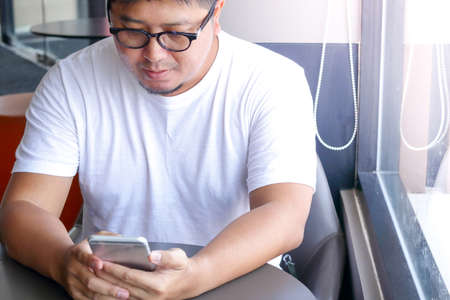 Men wearing glasses, wearing a fat white shirt. Pressing the phone in the restaurantの写真素材