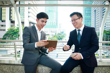 Two Asian men wearing a suit Is sitting and talking outside the officeの写真素材