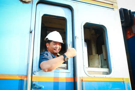 A young engineer worked on a train, wearing a white hat. Thumbs up. Performed various system checks.の写真素材