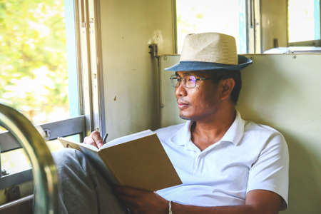 Men wear glasses, read books on the train. Traveling aloneの写真素材