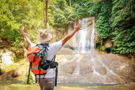 Asian tourists are walking in the forest to see beautiful waterfalls. Raise both hands with pleasure.の写真素材