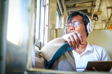 Men wearing glasses and wearing headphones Sitting eyes closed on the train Traveling aloneの写真素材