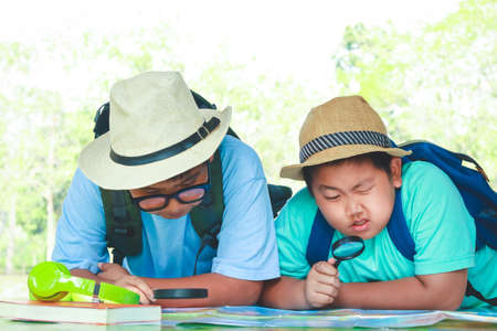 Two boys holding a magnifying glass. View the map. Concept of educationの写真素材