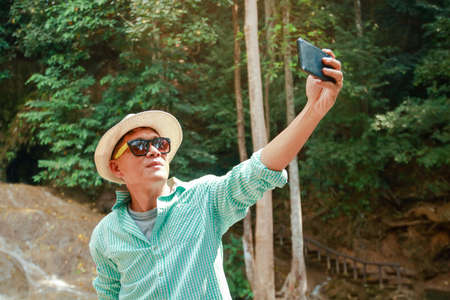 Asian tourists wear hats with sunglasses. Stand holding the phone, take a picture of yourselfの写真素材