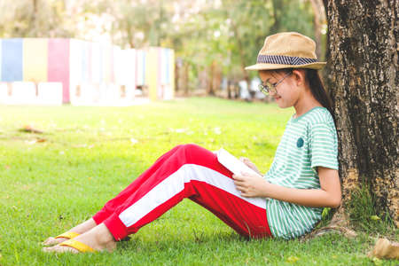 Asian schoolgirl wearing a hat She sat reading a book under a big tree.の写真素材