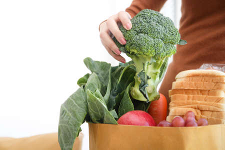 Young woman picks fresh vegetables from a brown paper bag. That order from online groceries Home delivery.の写真素材