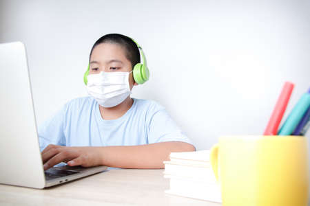Asian male students learn online from home through video calls, using their laptop computers to communicate with their teachers. Social distance to reduce the spread of the coronavirus (COVID-19).の写真素材