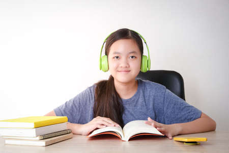 Asian female students learn online from home. Put on headphones and read a book. Concept of social distance Use of technology for education.の写真素材