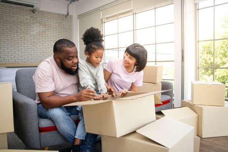 African American family moves to new home Help unpack the paper box. They are happy. The daughter...