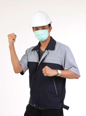 Asian engineer wearing a white safety helmet And wear a mask Act to raise your hands strong against virus and dust PM 2.5. Concept of industrial workers. White backgroundの写真素材