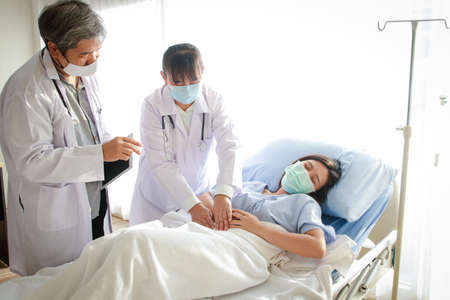 Two Asian doctors examined the abdominal pain of a woman lying in a hospital bed.の写真素材