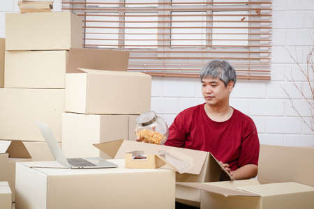 Fat man with white hair is packing products into paper boxes for delivery The concept of small entrepreneurs, online trading business, deliver goods by mailの写真素材