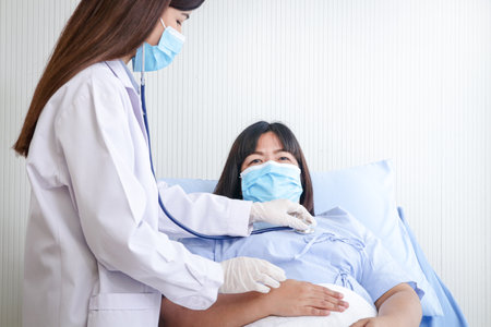Doctors used a stethoscope to examine the health of a fat woman, wearing a mask, lying on a hospital bed. Treatment of patientsの写真素材