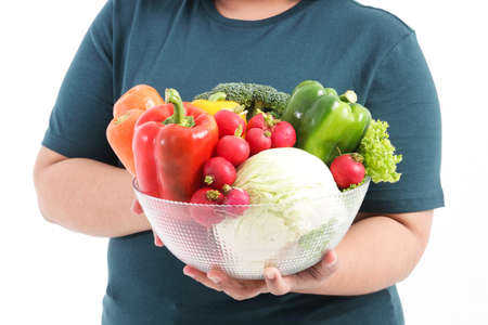 A fat woman holds fresh organic vegetables in a clear glass bowl. The concept of losing weight Eat healthy foods. White backgroundの写真素材