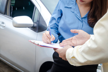 A woman driving a car has an accident during the rain. Signing the auto insurance claim document with an insurance agent. Concept a road trafficの写真素材