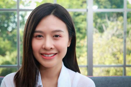 Woman beautiful white skin long hair asian Have a beautiful smile, look healthy. Sit on the sofa in the living room at home. The concept of health care for women in their 30s.の写真素材