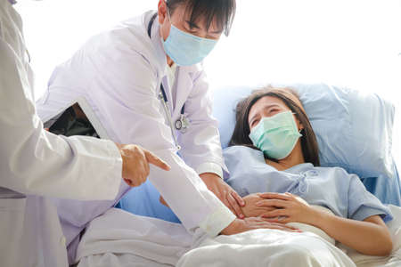 Two Asian doctors examined the abdominal pain of a woman lying in a hospital bed.