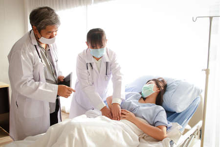 Two Asian doctors examined the abdominal pain of a woman lying in a hospital bed.の写真素材