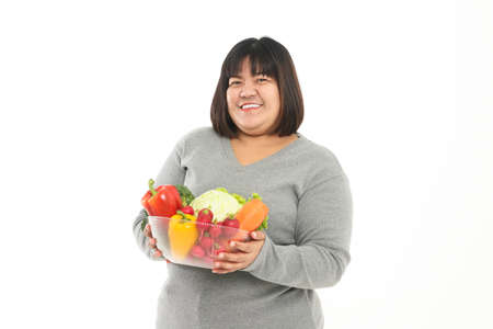 Fat Asian woman holding a bowl of fresh organic vegetables Food for good health. The concept of losing weight, reducing fat Healthy eating, nutrition, prescription food. White backgroundの写真素材