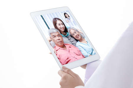 The concept of connecting with communication through online technology. A female doctor with a tablet Chat online, treat Asian elderly patients through video calls. White background.の写真素材